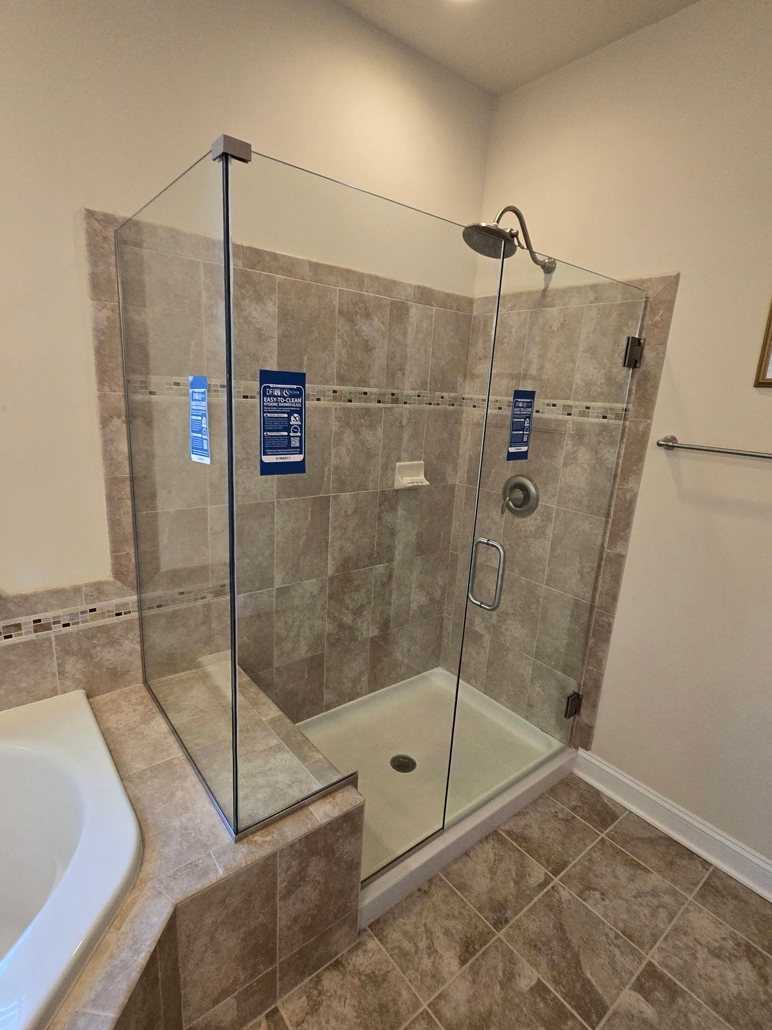 Walk-in shower with glass enclosure, beige tile, and chrome showerhead beside a bathtub.