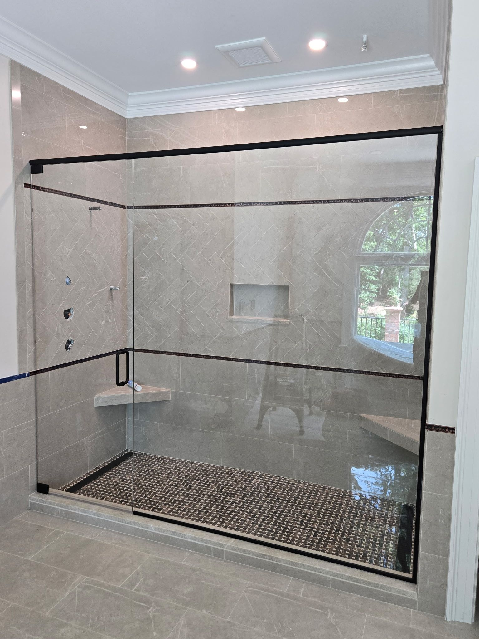 Glass-enclosed shower with black trim and mosaic tile floor in a modern bathroom