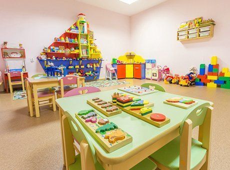 Child's playroom with tables, toys, and shelving unit shaped like a ship; pastel colors.