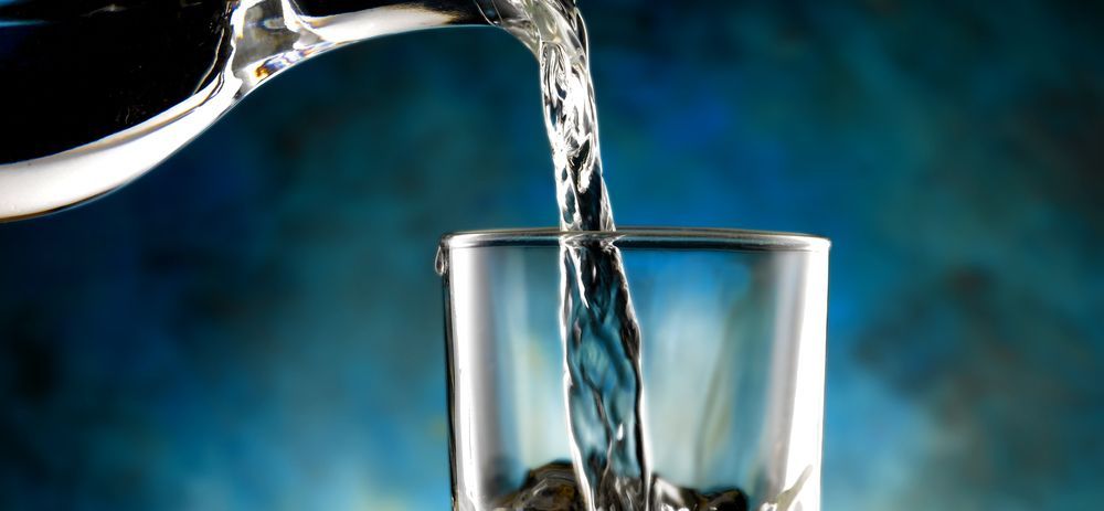 Water being poured into a clear glass against a blue background