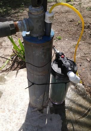 Wellhead pump and filtration tank with yellow hose outdoors on concrete.
