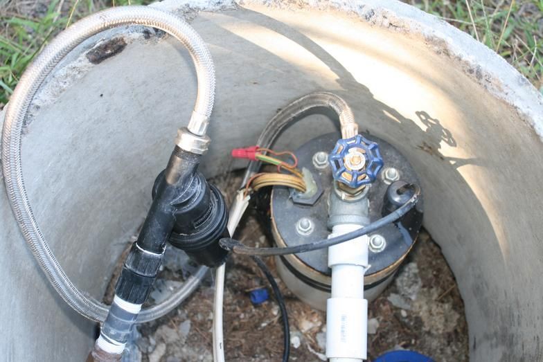 Interior of a well casing with pipes, hoses, and a pump control valve attached to a white PVC pipe.