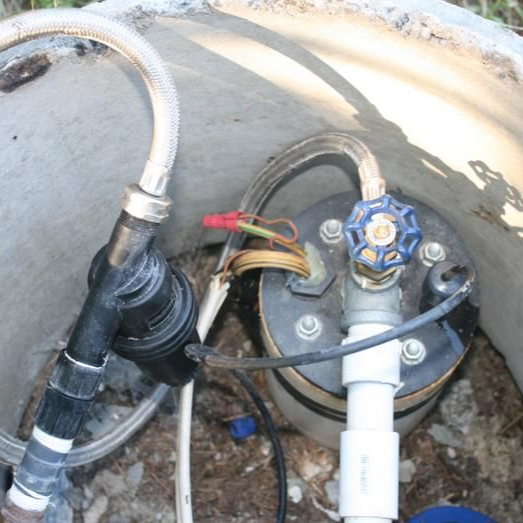 Interior of a well casing with pipes, hoses, and a pump control valve attached to a white PVC pipe.
