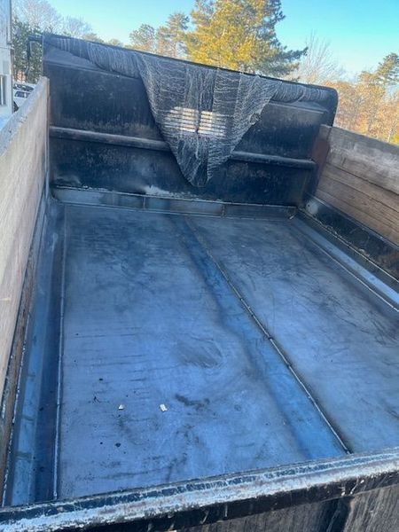 Inside of a dump truck bed with a black protective mesh cover, outdoors.