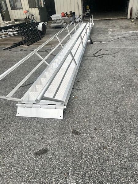 Aluminum ramp with stairs, railings, and landing on an asphalt surface.
