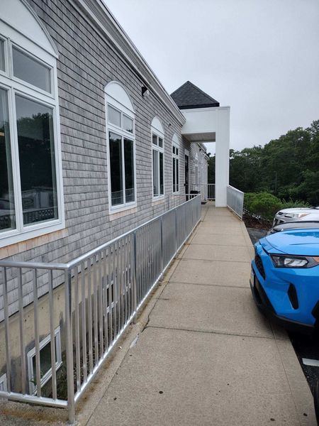 Gray building with a wheelchair ramp and silver railing, blue car parked nearby.