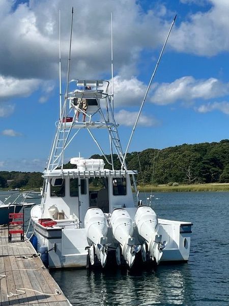 White sport fishing boat with three outboard motors docked at a pier, blue sky.