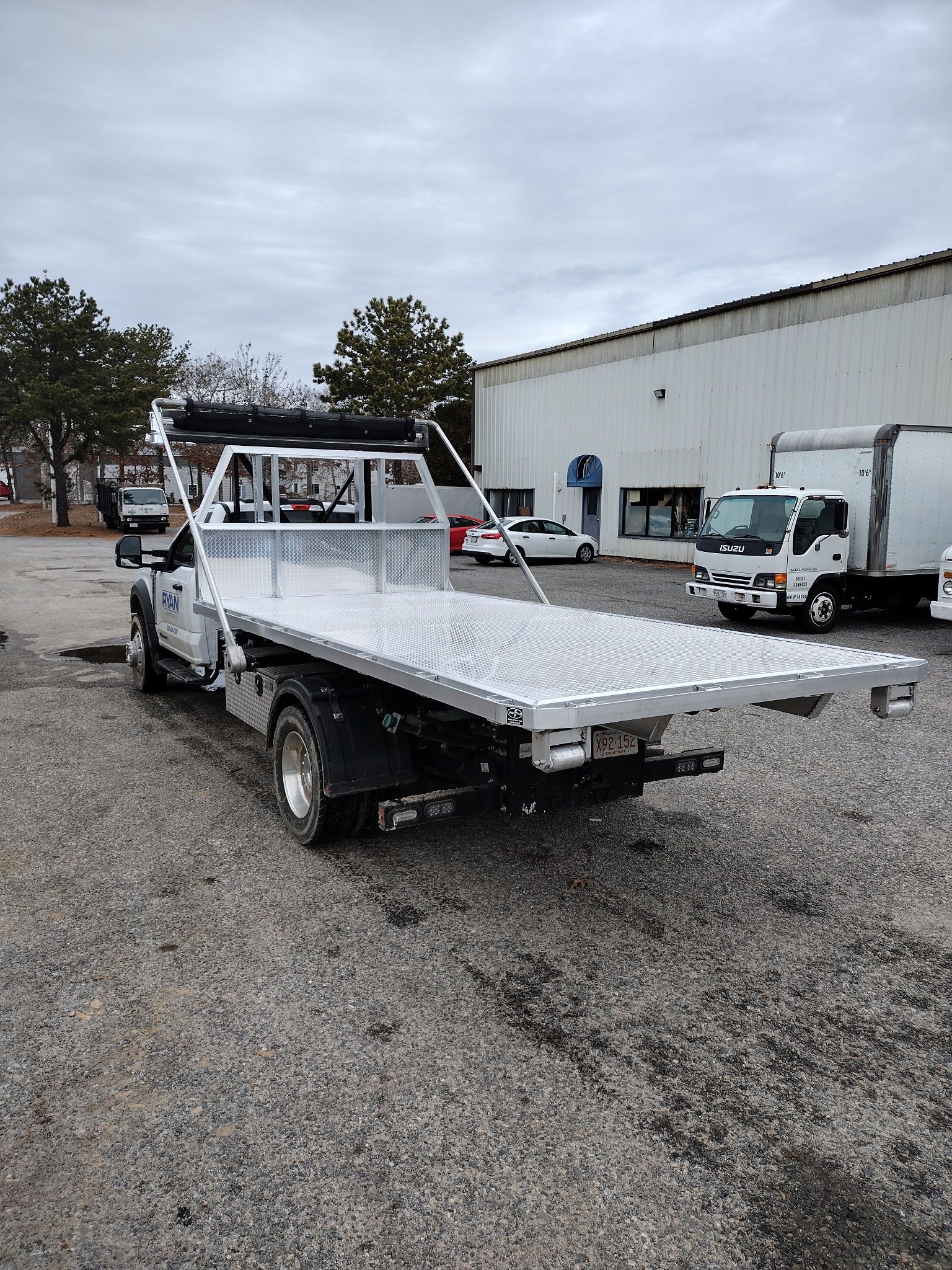Flatbed tow truck parked on gravel, with a building and other vehicles in the background.