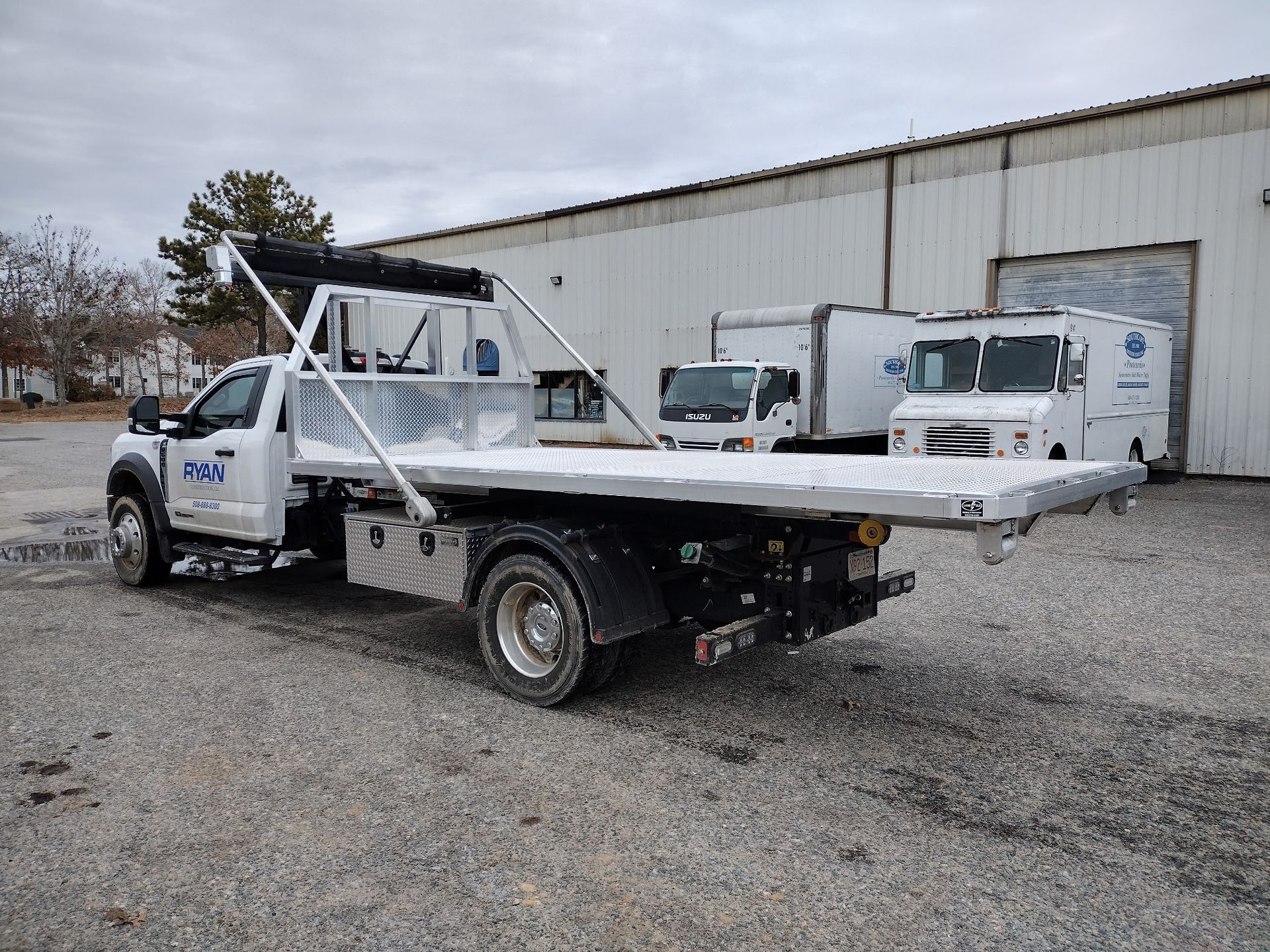 White tow truck on gravel, bed extended.  Building and other vehicles in background.