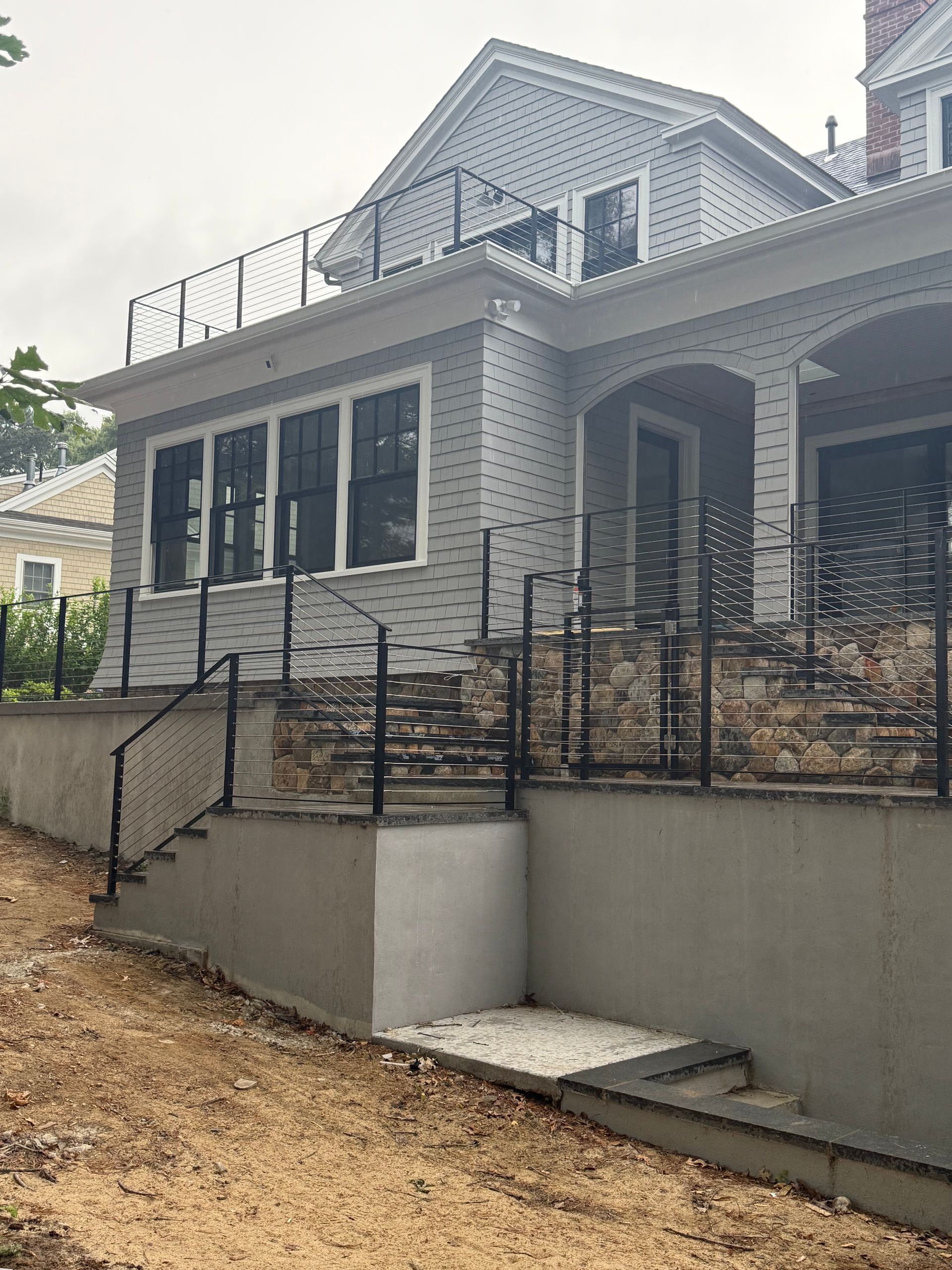 Exterior of a house with stone steps, black railings, and a gray facade under a cloudy sky.