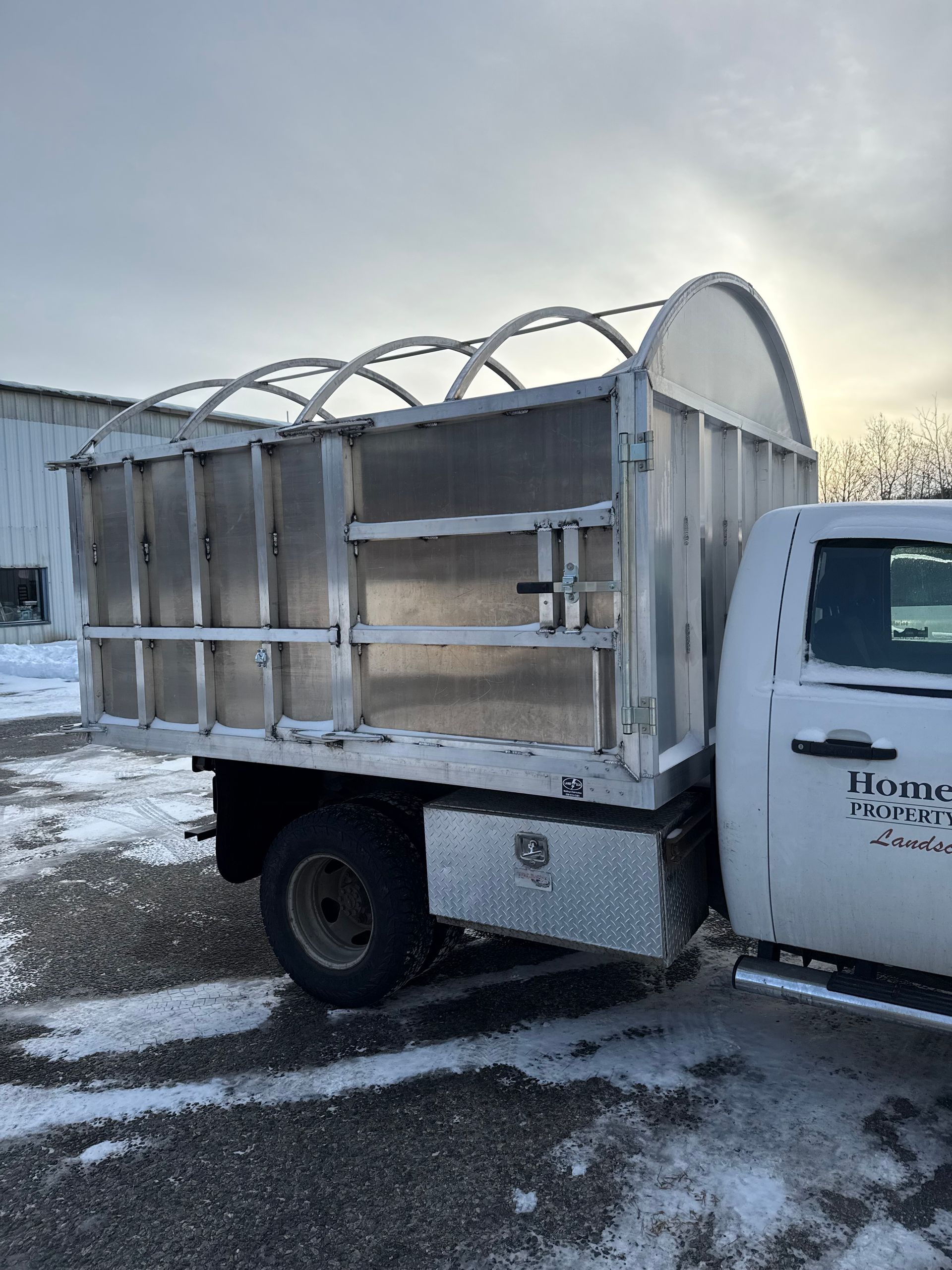 White pickup truck with a large, enclosed, silver-colored bed; snowy ground.
