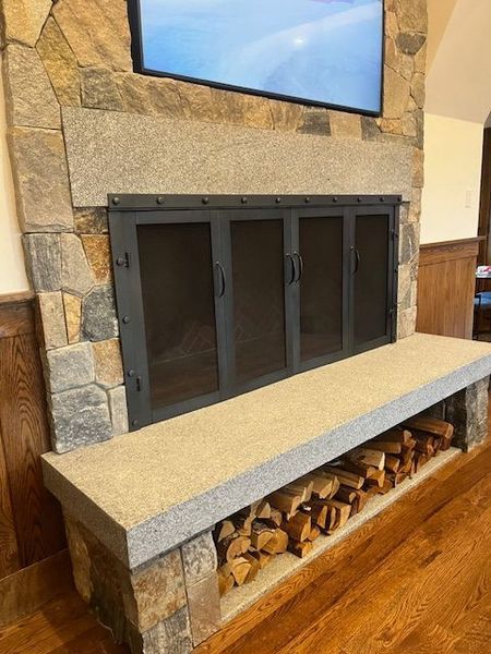 Stone fireplace with black screen doors, wood bench, and firewood storage.