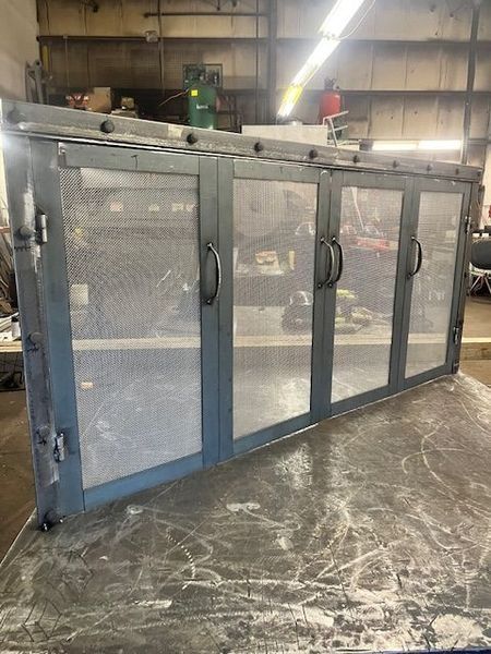 Metal cabinet with four screened doors, sitting on a table in a workshop.