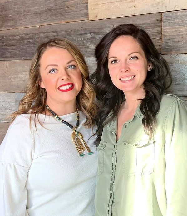 Two women are posing for a picture in front of a wooden wall.