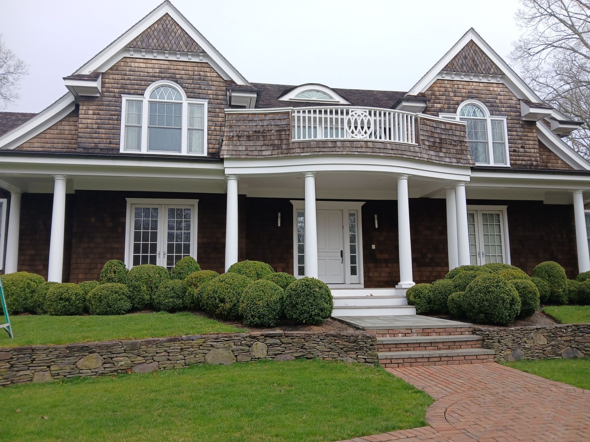 Large brick house with white trim, front porch, and manicured lawn under a cloudy sky.