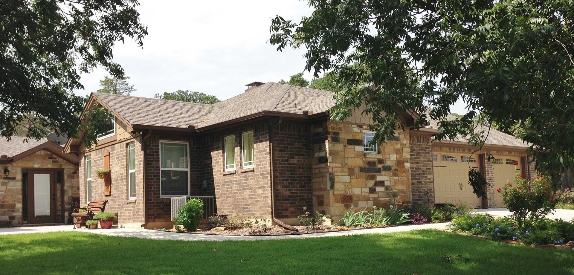 A brick house with a brown roof surrounded by trees