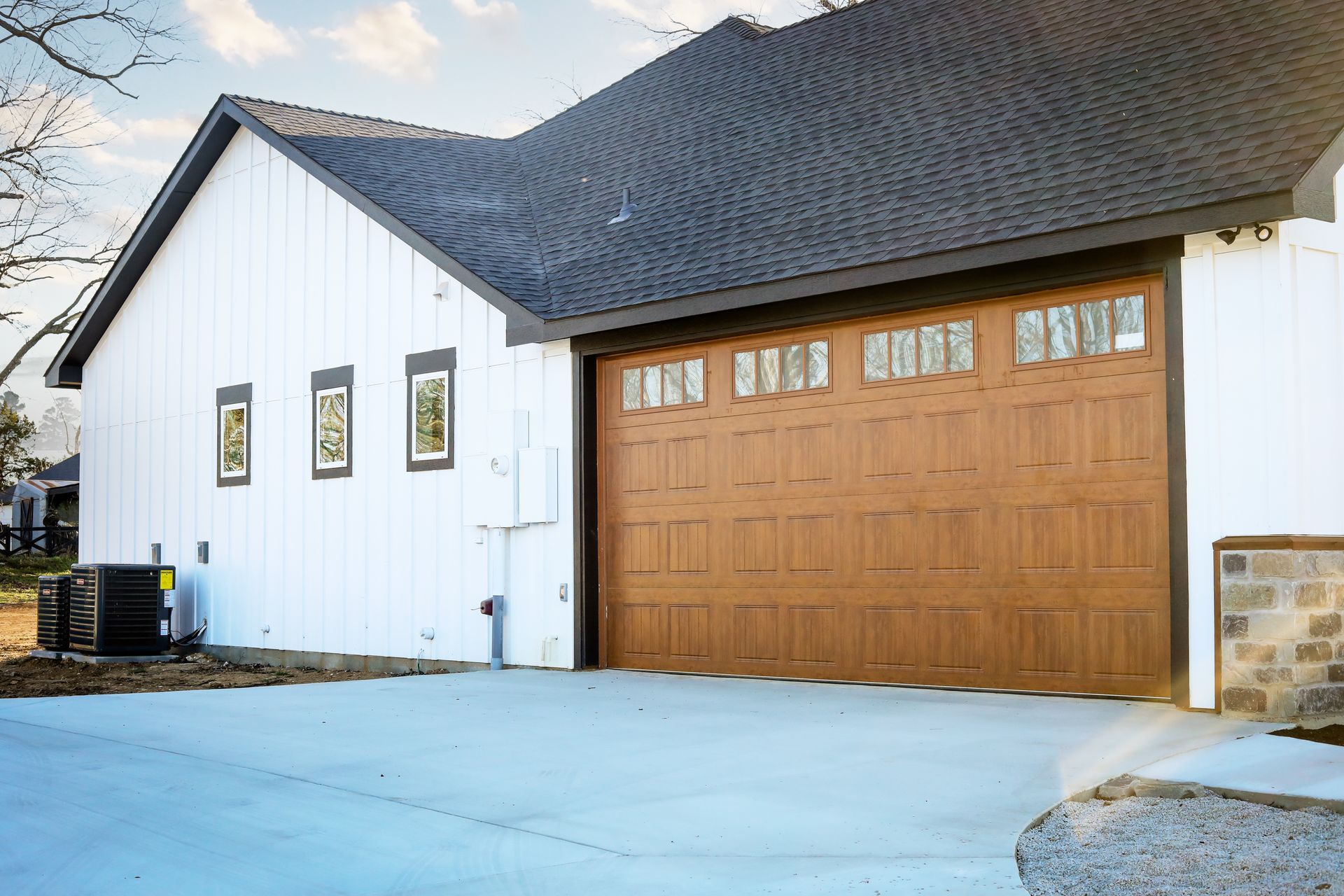 A white house with a brown garage door and a black roof.