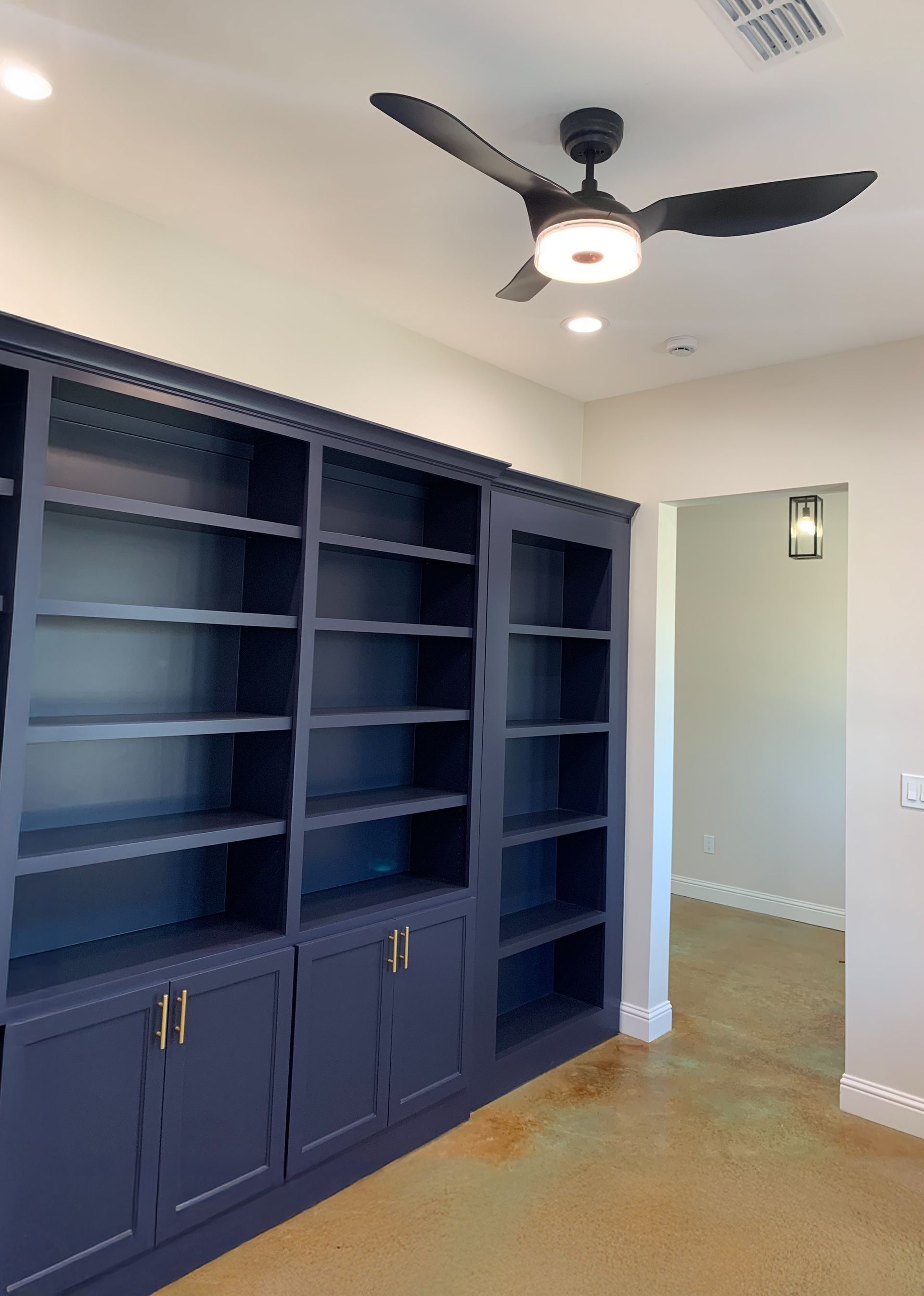 A room with a ceiling fan and a lot of shelves