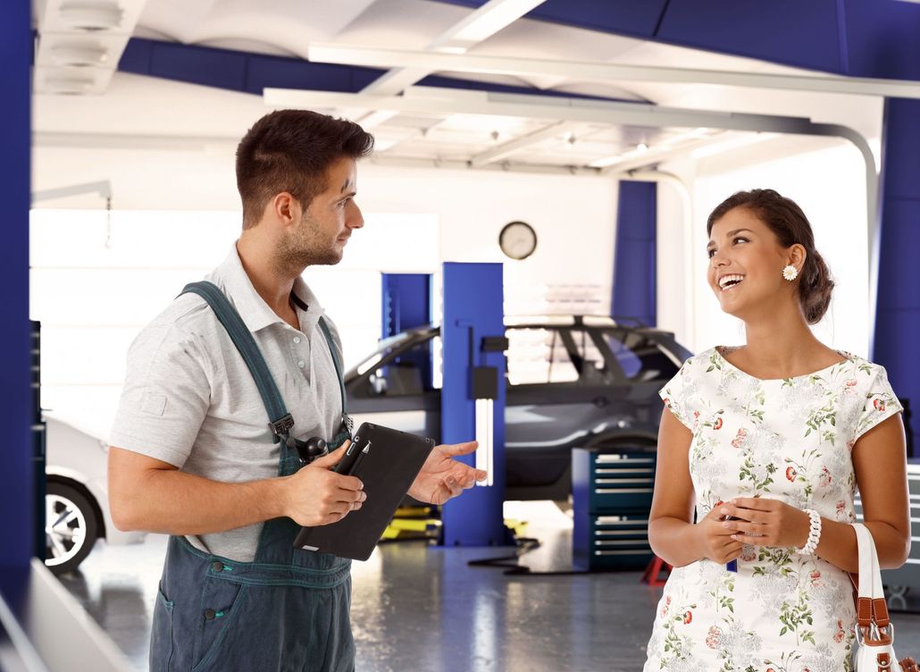 Two people talking in an auto repair shop with a blue car on a lift nearby