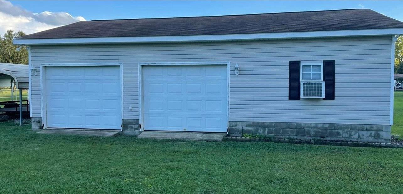A white garage with two doors, a window with shutters, and green grass.