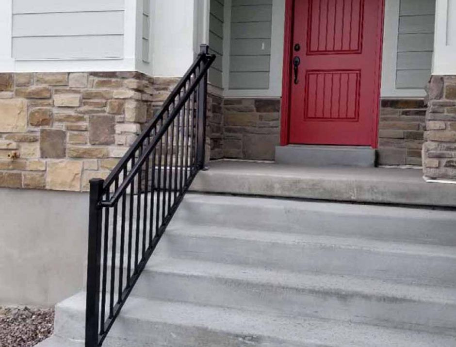 A red door with a black railing is on the front of a house.