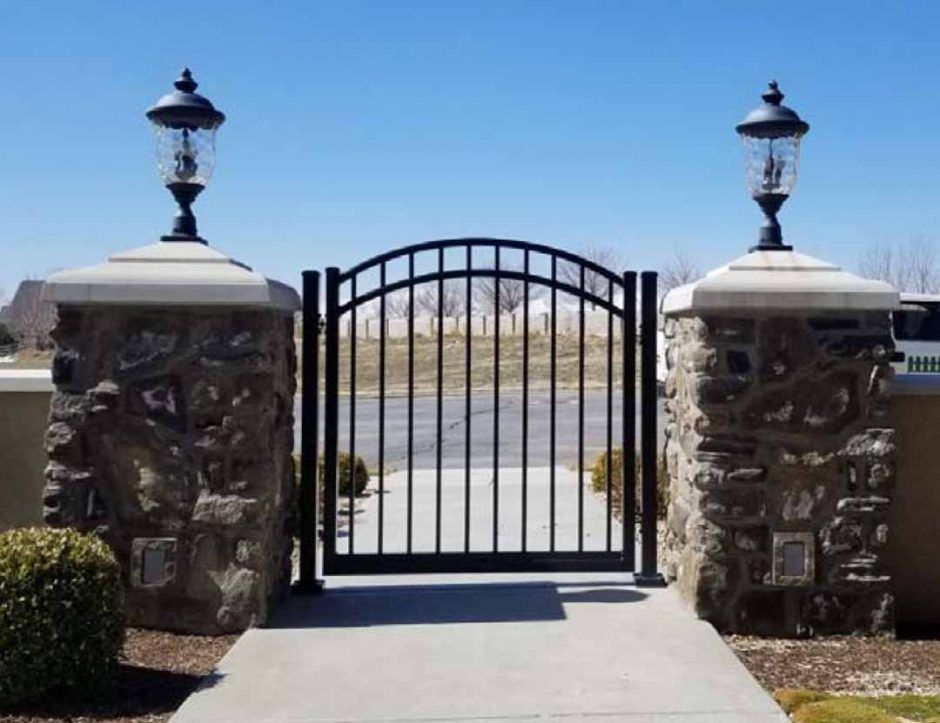A black gate is surrounded by stone pillars and lamps.