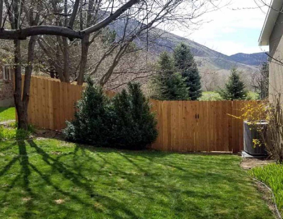 A wooden fence surrounds a lush green yard with mountains in the background.