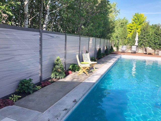 A fence surrounds a large swimming pool in a backyard.