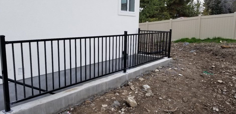 A black fence is sitting next to a white house.