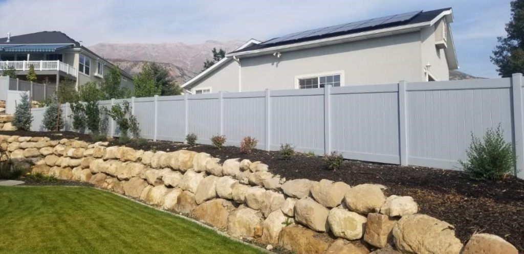 A white fence surrounds a rock wall in a backyard.