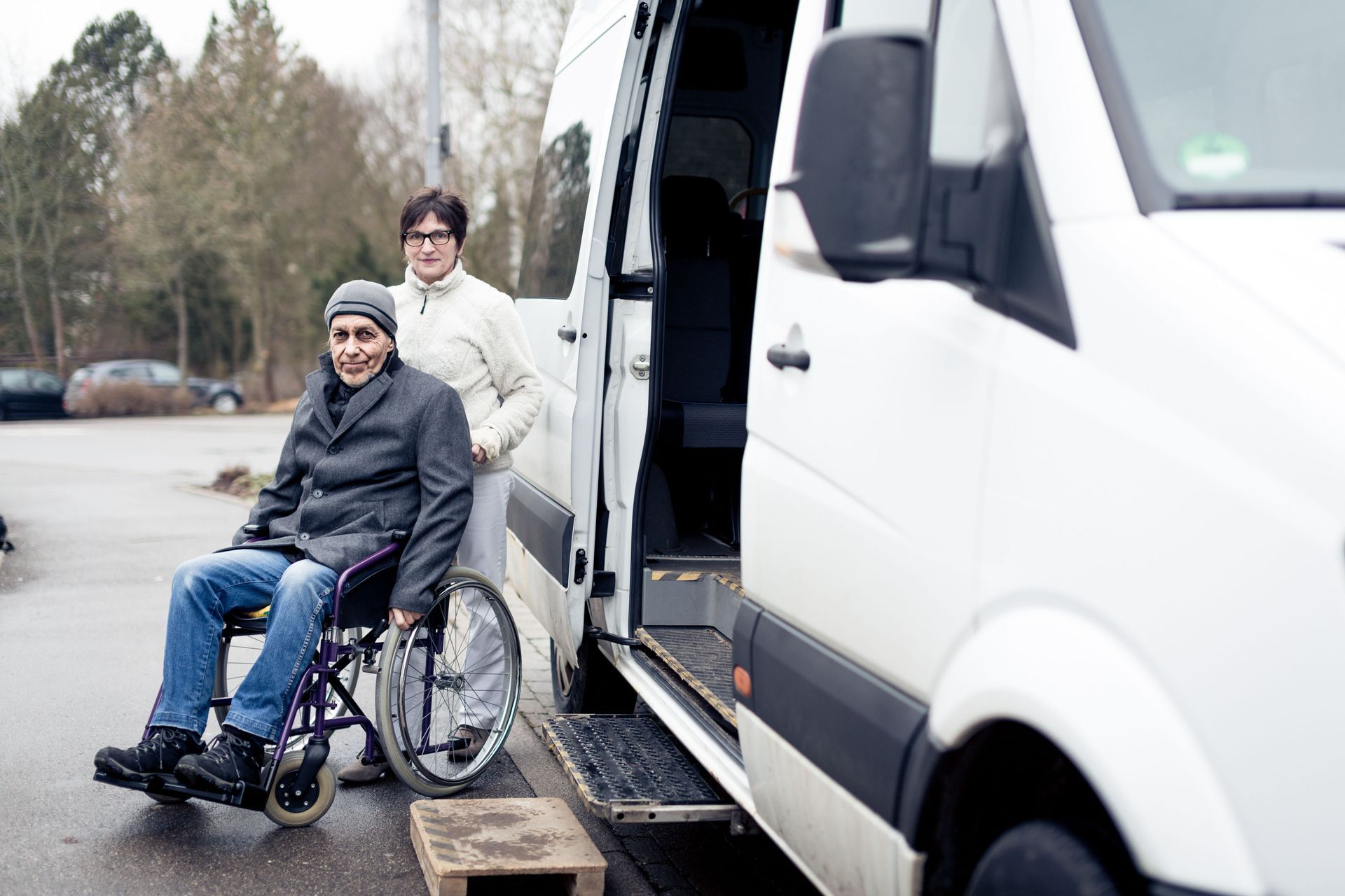A woman is helping a man in a wheelchair into a van.