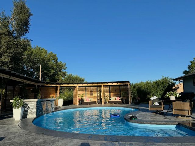 Pool area with blue water, seating, and a wooden pergola under a clear, bright sky.