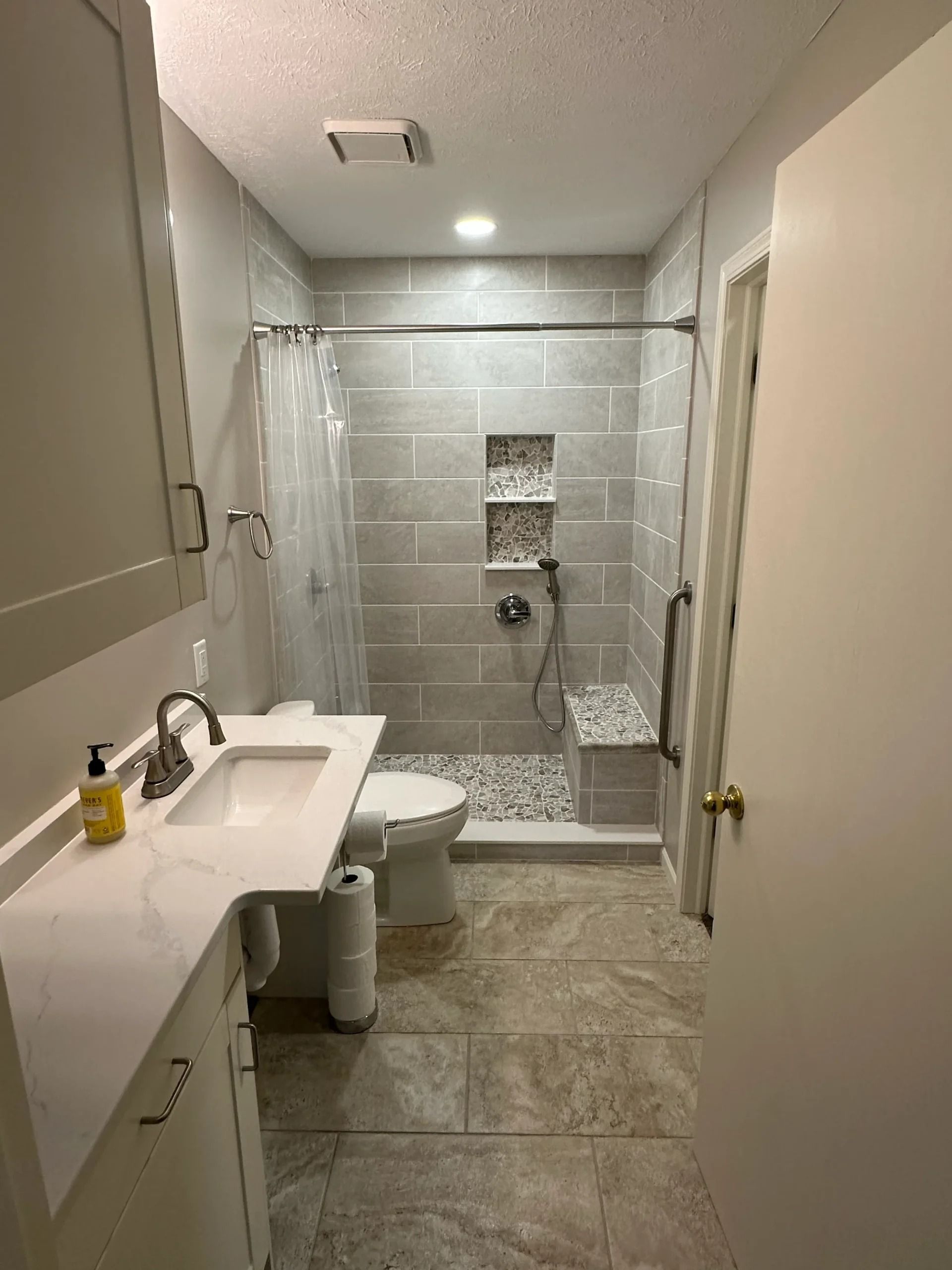 Bathroom with gray tiled shower, white vanity, and grab bar for accessibility.