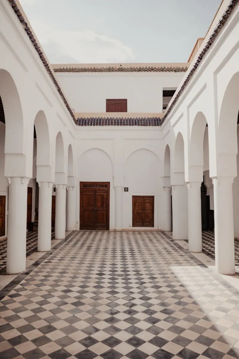 Courtyard with checkered floor, white arches, and wooden doors.
