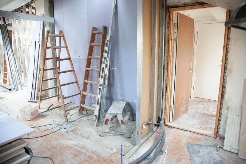 Room under renovation with ladders, plasterboard, and an open door.