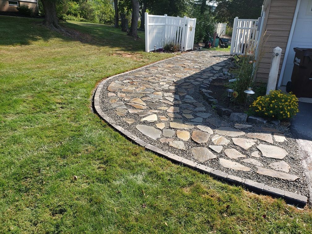 A stone walkway curves through a lawn, bordered by gray pavers and edged with loose gravel.