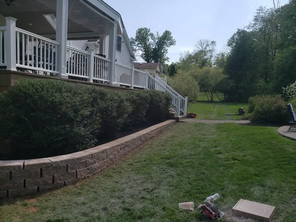 A tiered retaining wall with landscaping and a white deck railing in a residential backyard.