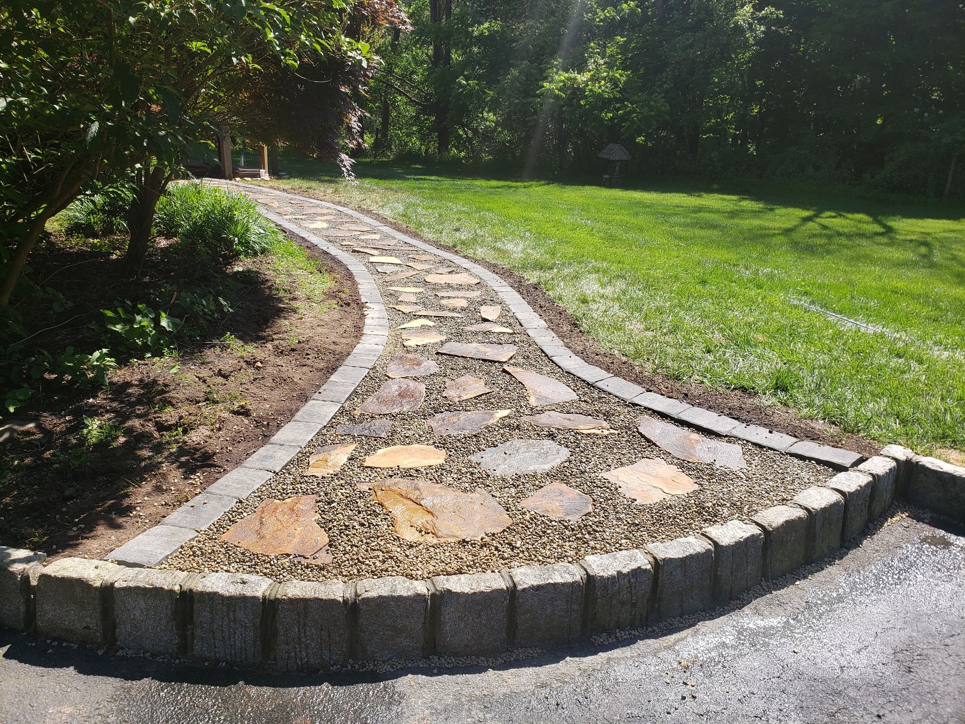 A stone garden path with curved stone edging leads from a paved area into a green lawn.