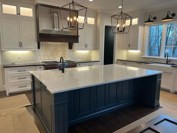 Modern kitchen with large navy island, white cabinets, pendant lights, and quartz countertop