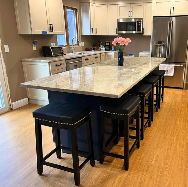 Modern kitchen with large marble island, black stools, stainless appliances, and a vase of pink flowers