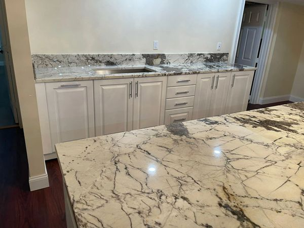 Modern kitchen with white cabinets, marble countertops, and dark wood flooring
