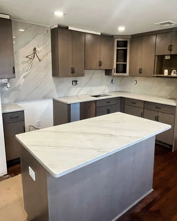 Modern kitchen with gray cabinets, white marble counters, and a central island with waterfall edge.