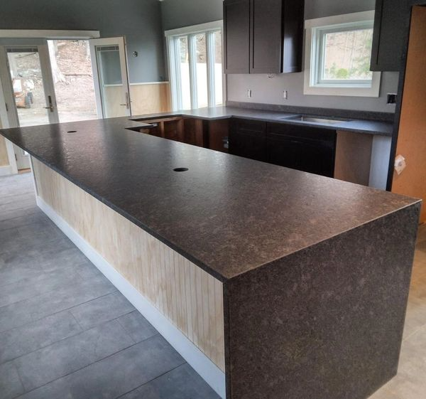 Empty modern kitchen with dark countertops, large island, tiled floor, and windows letting in natural light