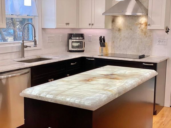 Bright modern kitchen with dark cabinets, light countertops, central island, and stainless steel range hood