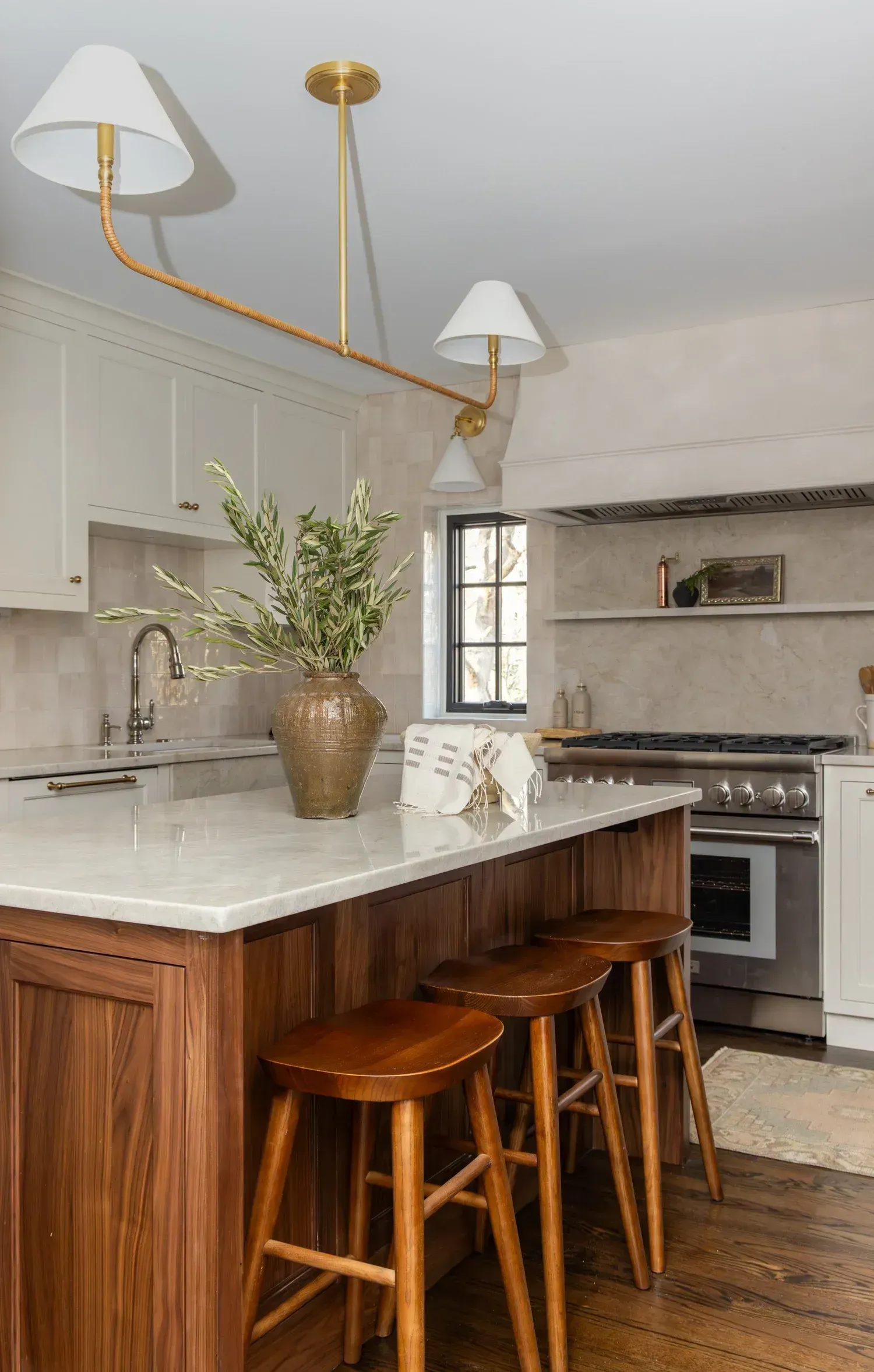 Bright kitchen with white cabinets, marble island, wood stools, and brass pendant lights