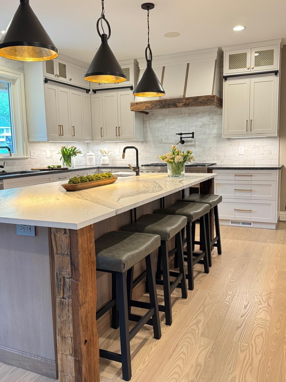 Modern kitchen with large island, dark pendant lights, white cabinets, and bar stools