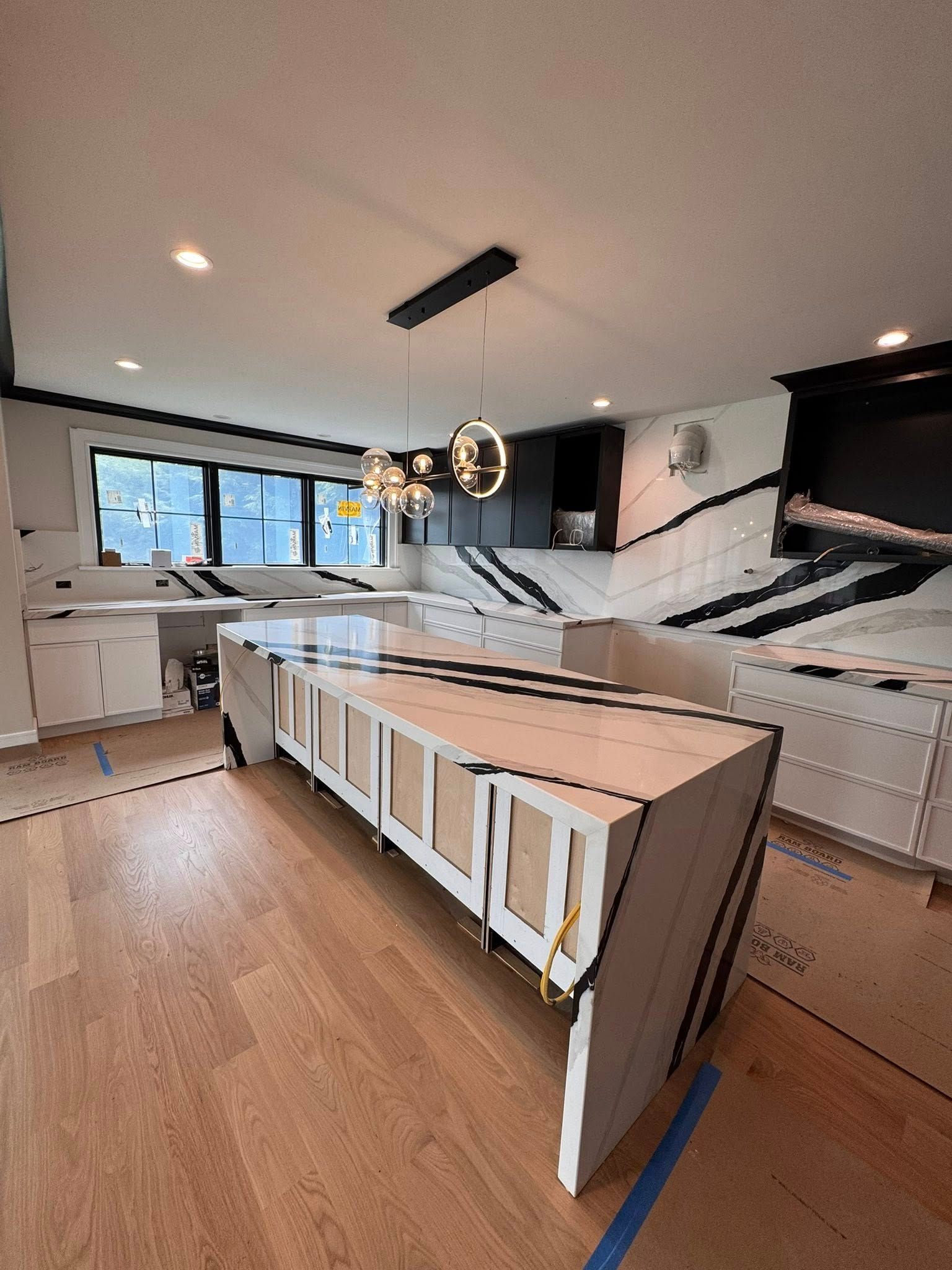 Modern kitchen under renovation with cabinets, island, wood floor, and hanging light fixture