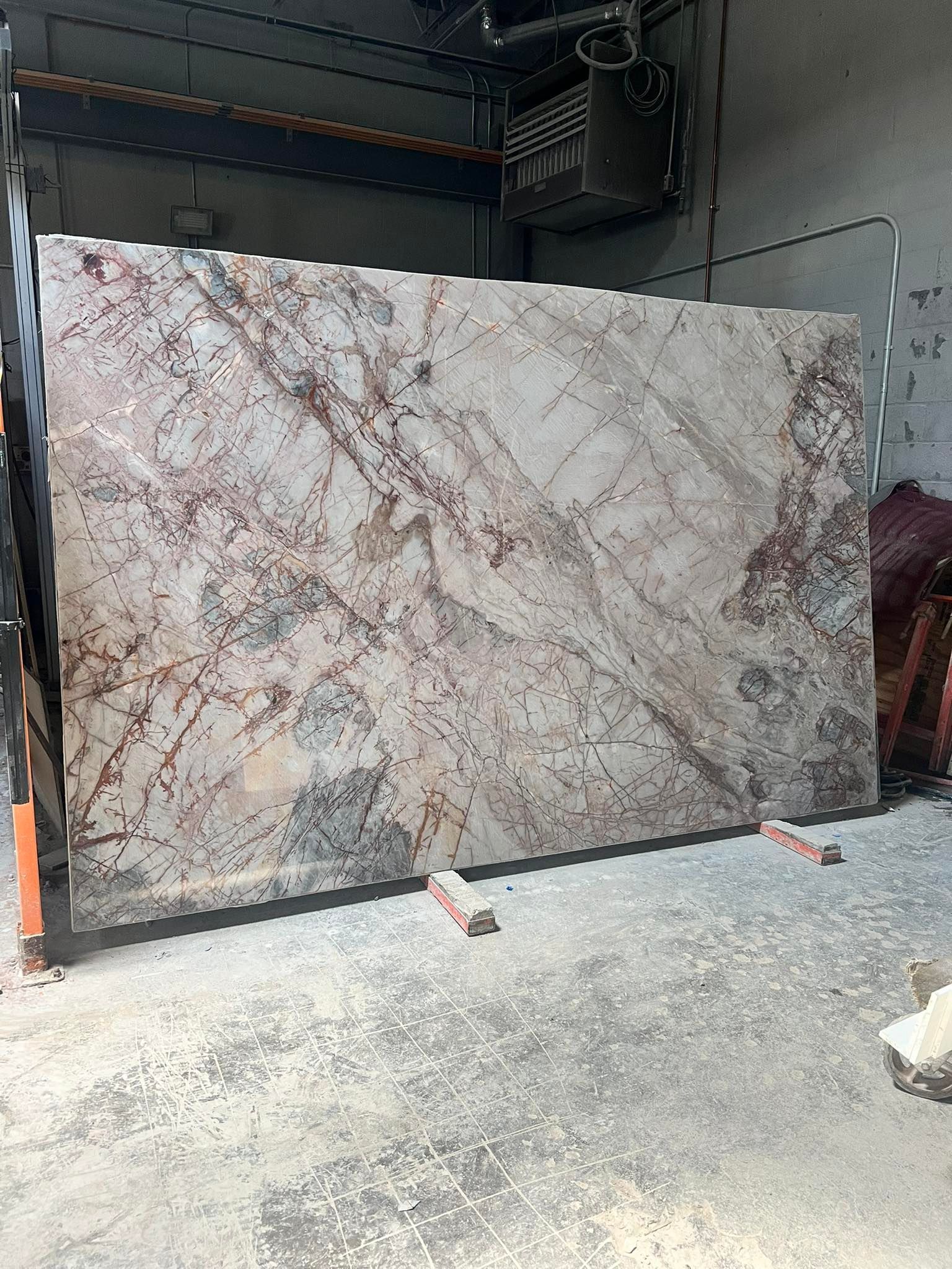 Large light-gray stone slab with pink veining stored upright in an industrial warehouse.