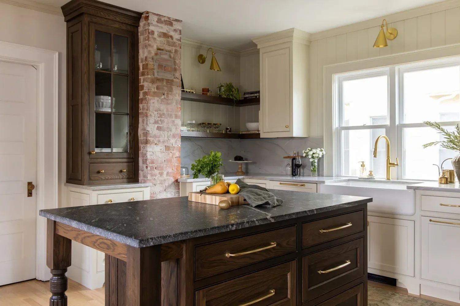 Bright kitchen with dark wood island, white cabinets, brick accent wall, and sunlight at the window