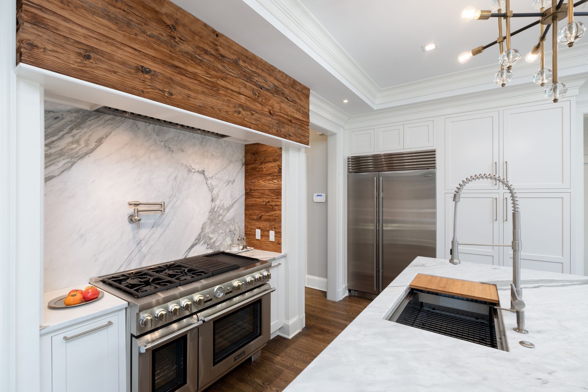 Modern white kitchen with marble island, stainless steel range, and wood-accented backsplash